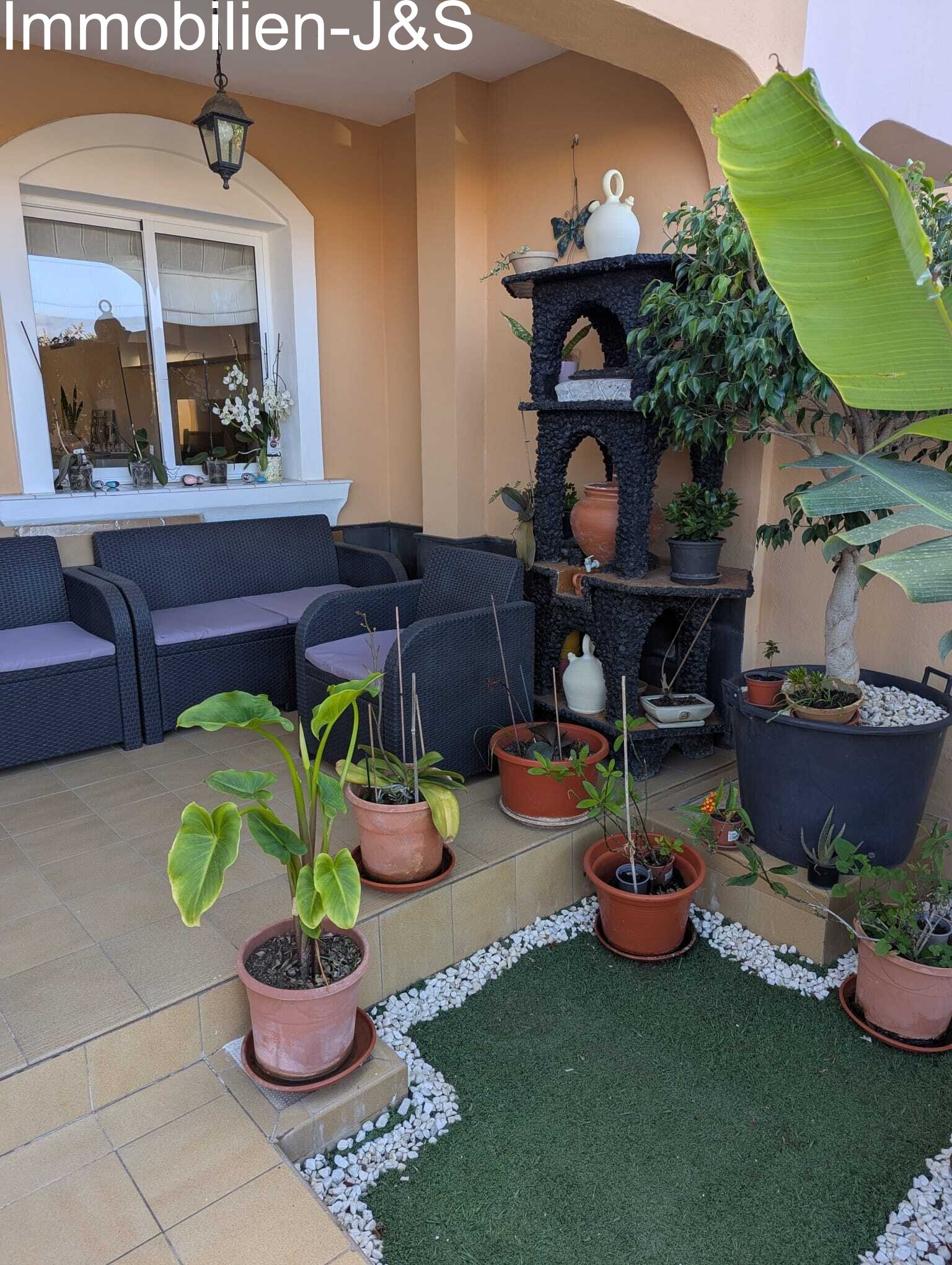 Gemütliche, überdachte Terrasse mit komfortabler Rattan-Sitzgruppe, liebevoller Bepflanzung und einem dekorativen, vulkanisch anmutenden Steinregal für ein authentisches kanarisches Ambiente. Gemütliche, überdachte Terrasse mit komfortabler Rattan-Sitzgruppe, liebevoller Bepflanzung und einem dekorativen, vulkanisch anmutenden Steinregal für ein authentisches kanarisches Ambiente.