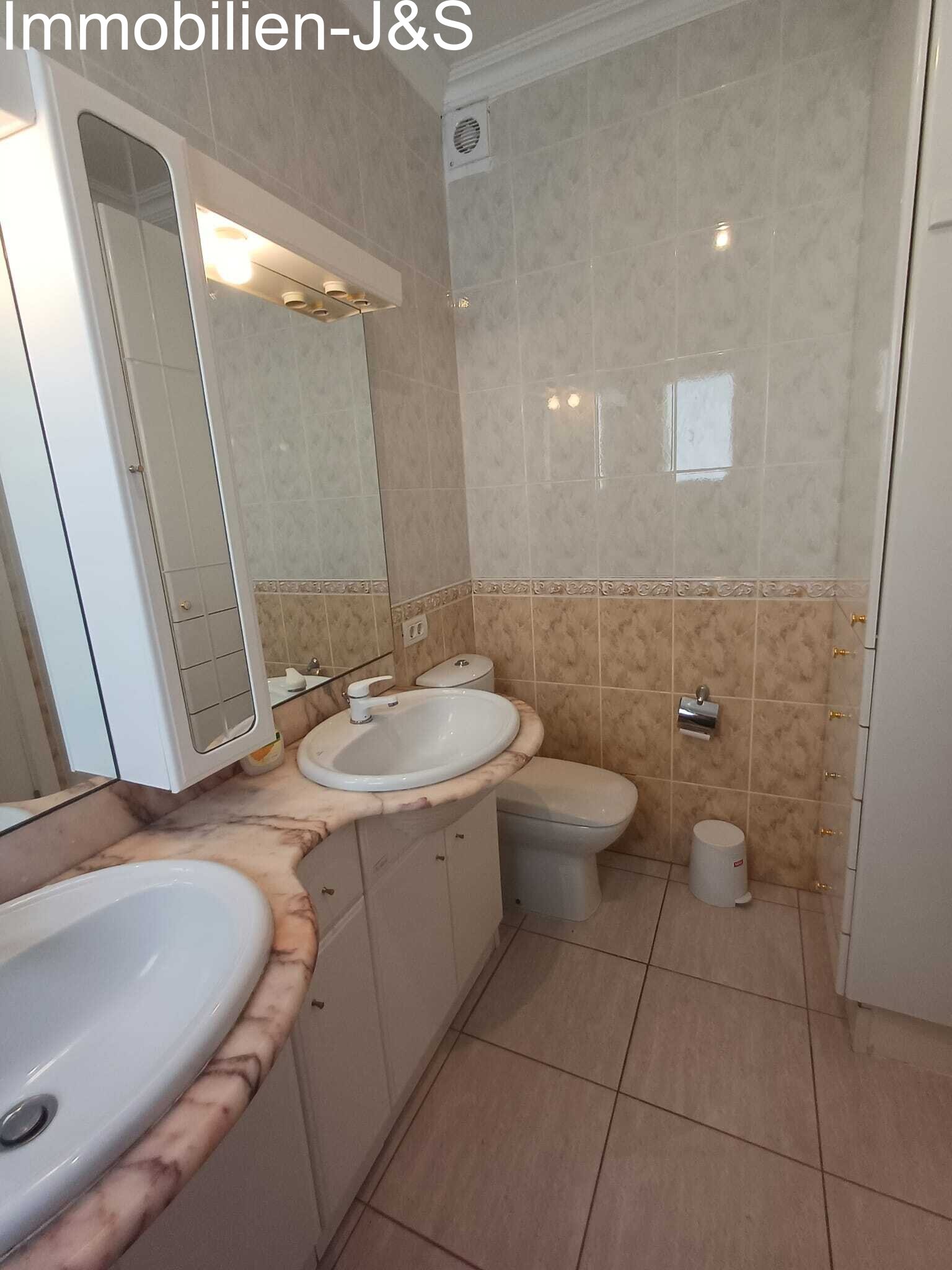 Klassisch gefliestes Badezimmer mit Doppelwaschbecken, großem Spiegel und praktischen Einbauschränken.