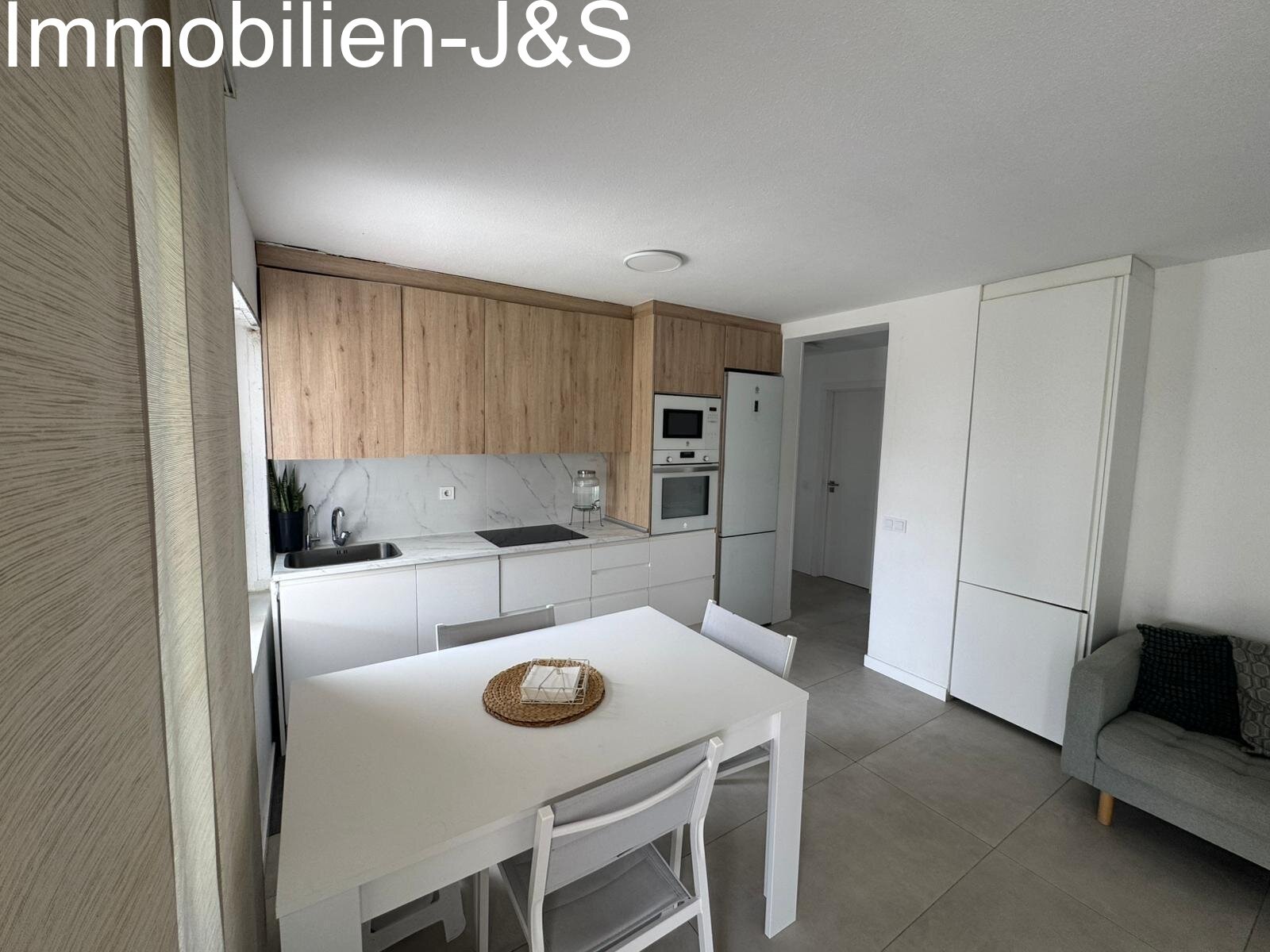 Moderne, offene Küche in edler Holz-Optik und Weiß. Voll ausgestattet mit hochwertigen Einbaugeräten und einem integrierten Essbereich – funktional, hell und perfekt in den Wohnraum integriert.