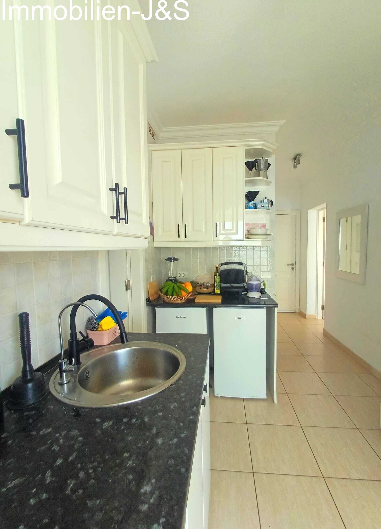 Cocina equipada funcional y luminosa de estilo rústico con encimera oscura y mucho espacio de almacenaje, conectada directamente con el pasillo abierto.