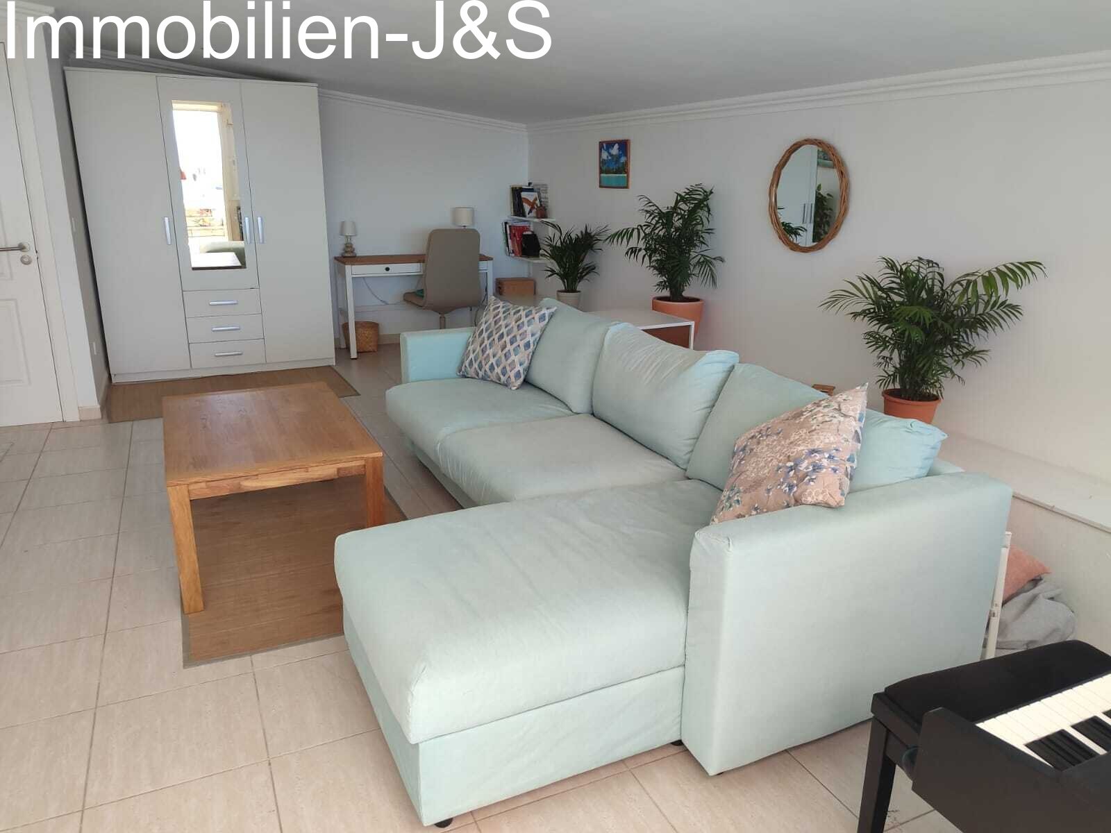 Zona de estar moderna con un amplio sofá rinconera en verde menta suave, combinado con muebles de madera clara y plantas naturales para un ambiente acogedor.