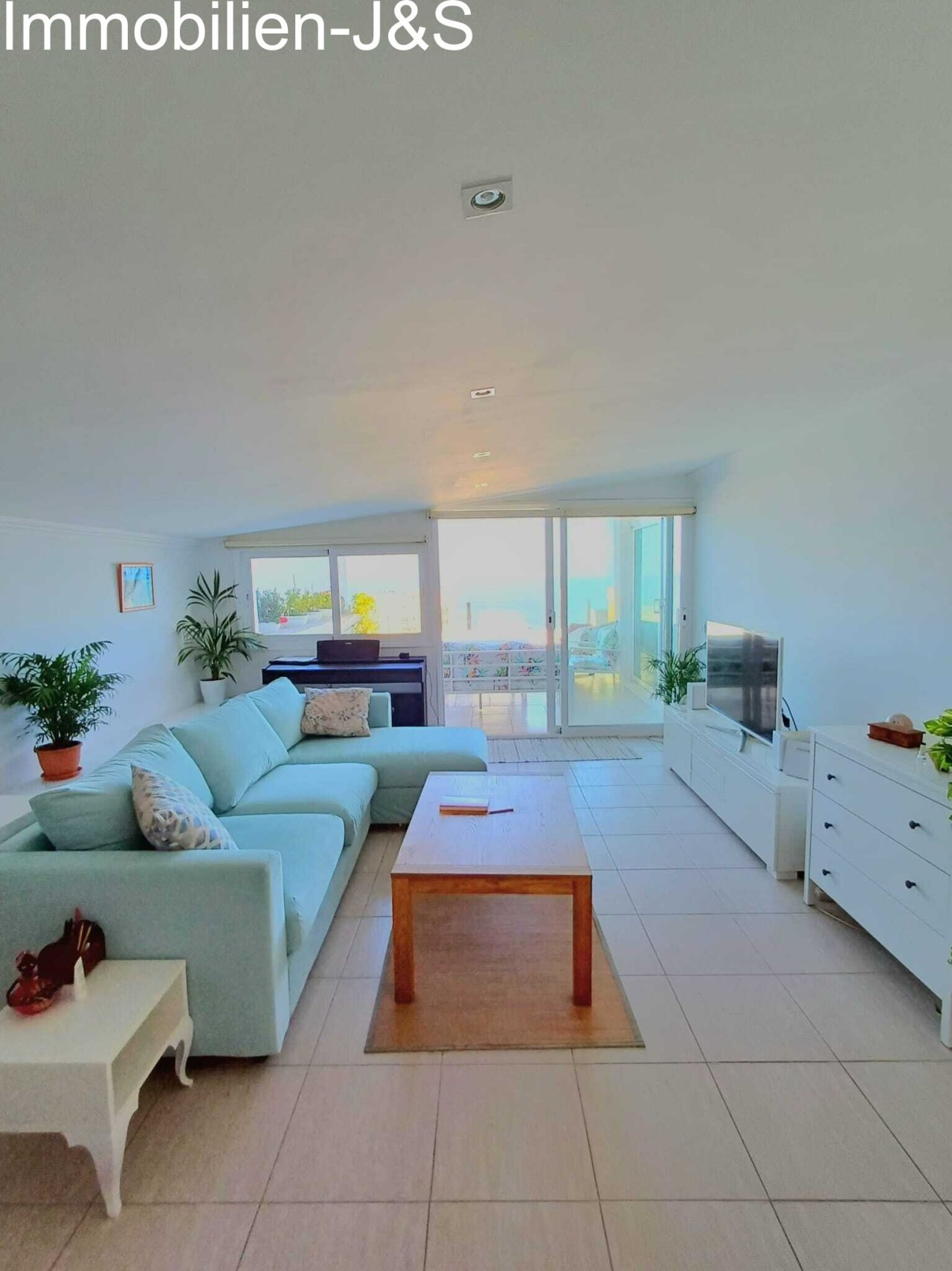 Zona de estar moderna con un amplio sofá rinconera en verde menta suave, combinado con muebles de madera clara y plantas naturales para un ambiente acogedor.