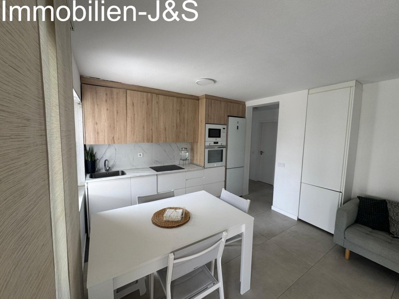 Moderna cocina abierta con elegantes acabados en madera y blanco. Totalmente equipada con electrodomésticos integrados de alta calidad y una zona de comedor: funcional, luminosa y perfectamente integrada en el salón.