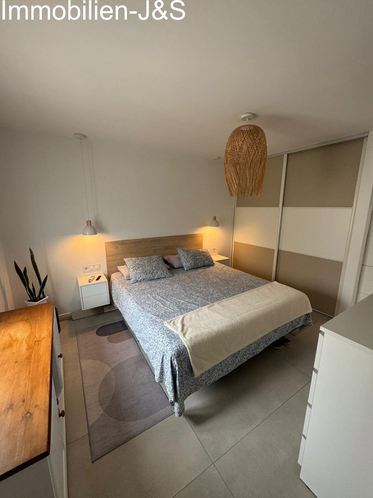 Un dormitorio acogedor con un toque natural. El diseño destaca por sus cálidos detalles en madera, modernas lámparas colgantes y una iluminación armoniosa que crea un ambiente relajante.